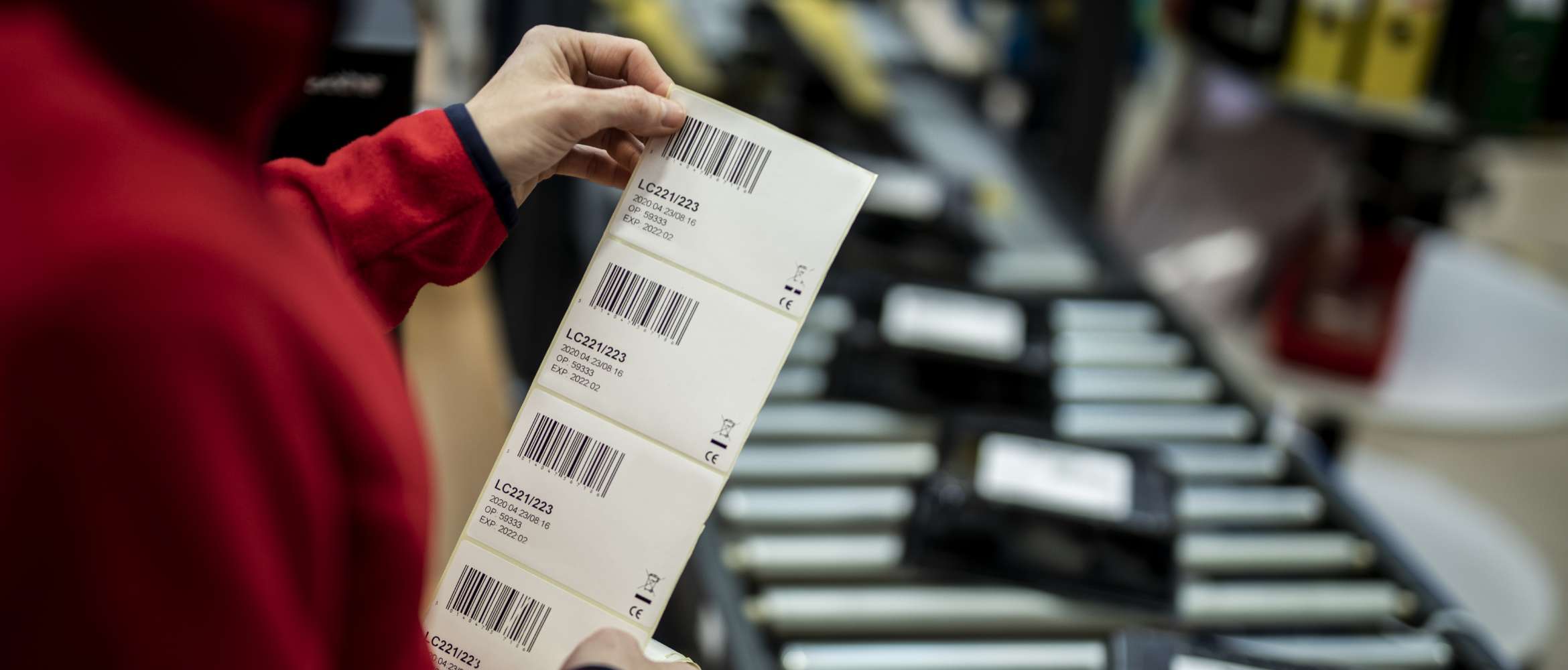 A worker on a factory line in a distributed manufacturing and logistics operation is inspecting a printed barcode label before attaching it to a package. 